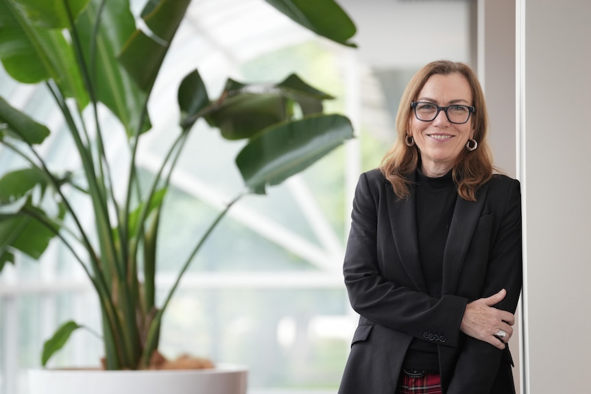 Professor Nicole Gurran from Sydney University leans on a wall inside a room while looking at the camera.