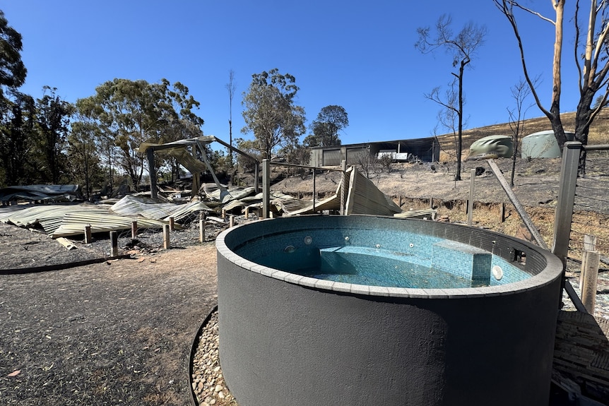 A hot tub stands in front of a burnt out house
