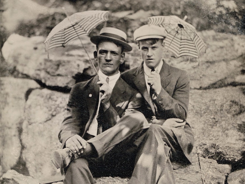 Two men sitting together holding small umbrellas.