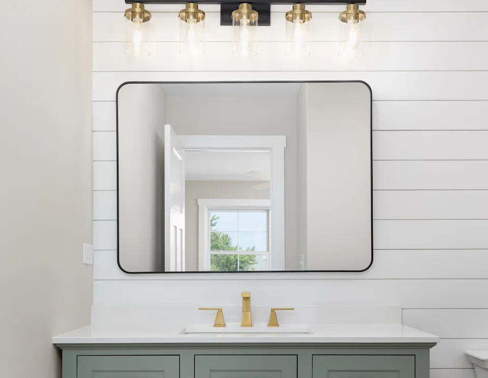 Modern bathroom with shiplap walls, a rectangular mirror, vanity with brass fixtures, six-light fixture, and a green cabinet with white countertop