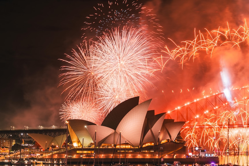 The large white sail-like structures of the Sydney Opera House are illuminated by red fireworks.