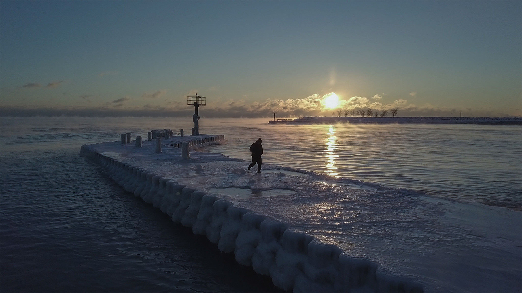 A man walks along an icy breakwater at sunrise at...