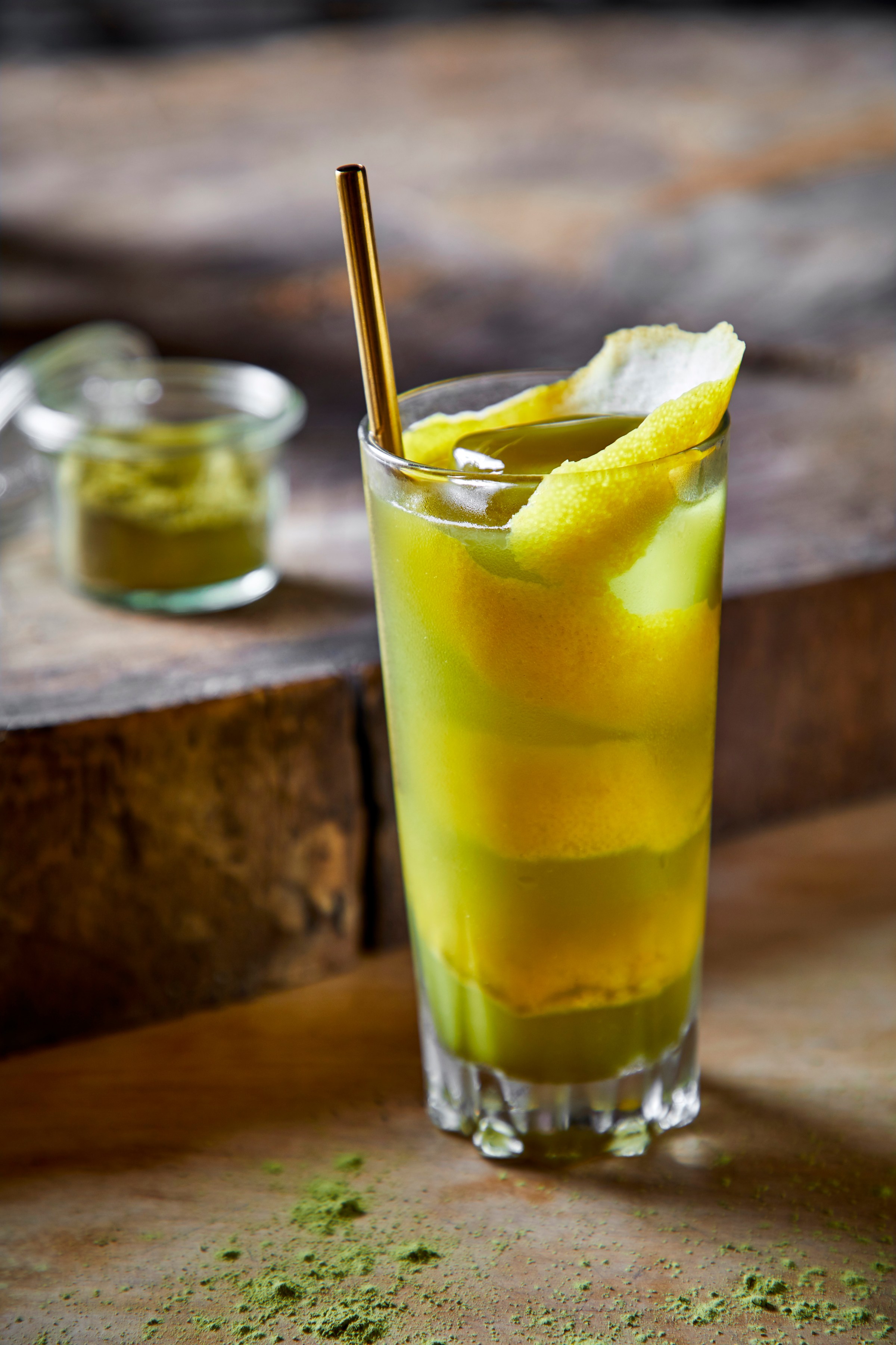 A cocktail in a tall glass with a swirl of lemon rind and a metal straw.