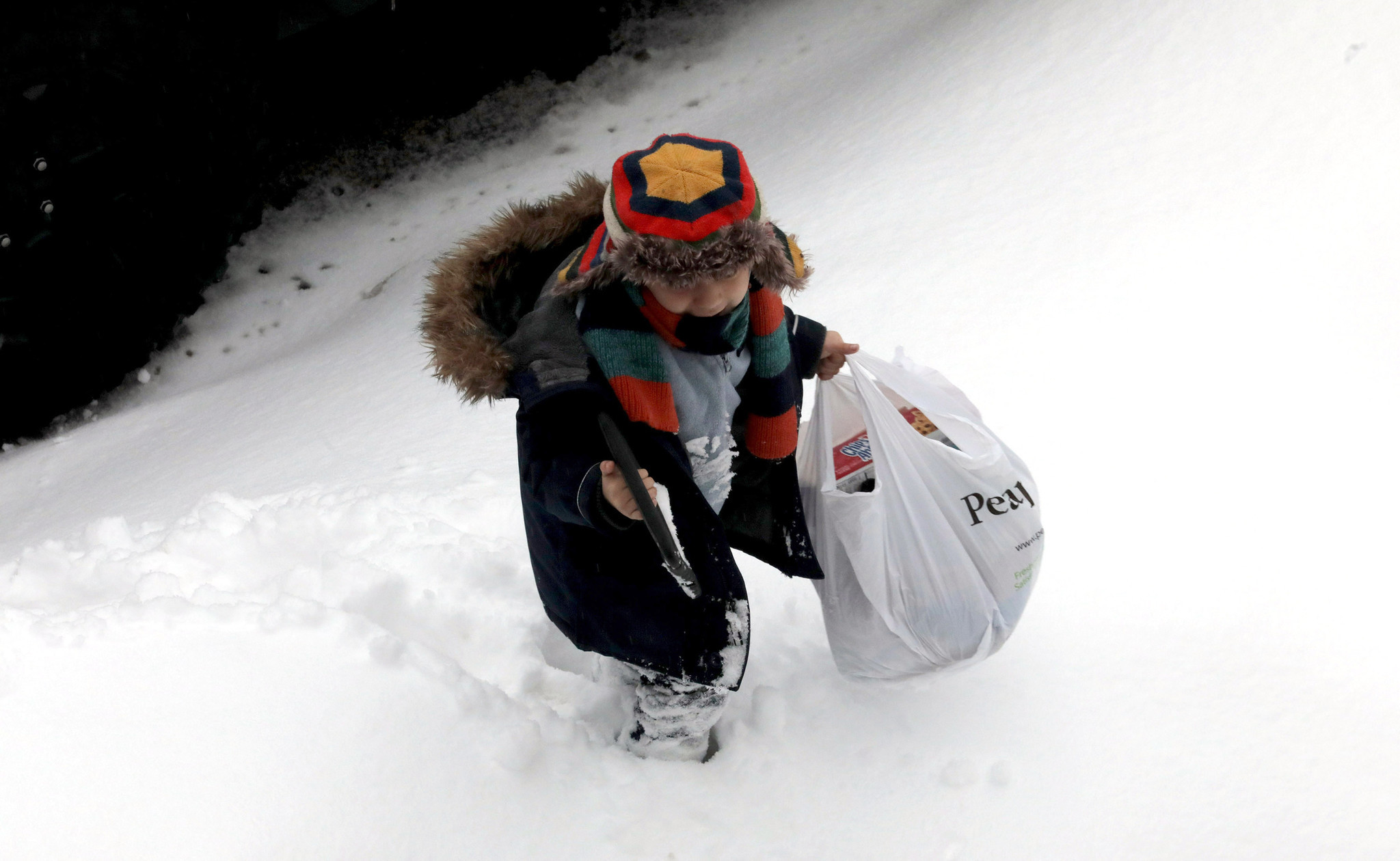A young boy trudges through the snow with shopping bags...