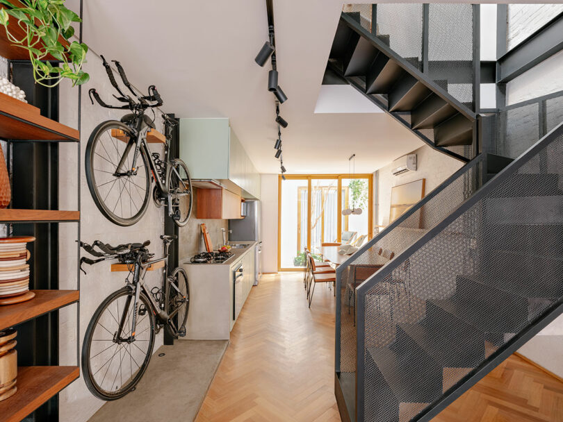 Modern kitchen and dining area with two bicycles mounted on the wall, open shelving, and a black metal staircase leading to an upper floor.