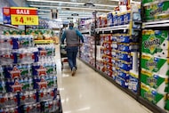 A shopper walks past cases of water along with toilet paper and paper towels at a Kroger on...