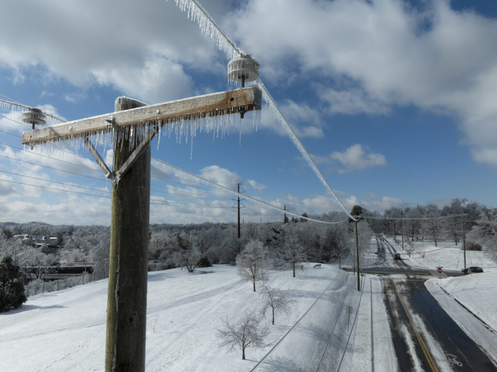 Utility lines with ice stretch over a snowy scene with a plowed road.