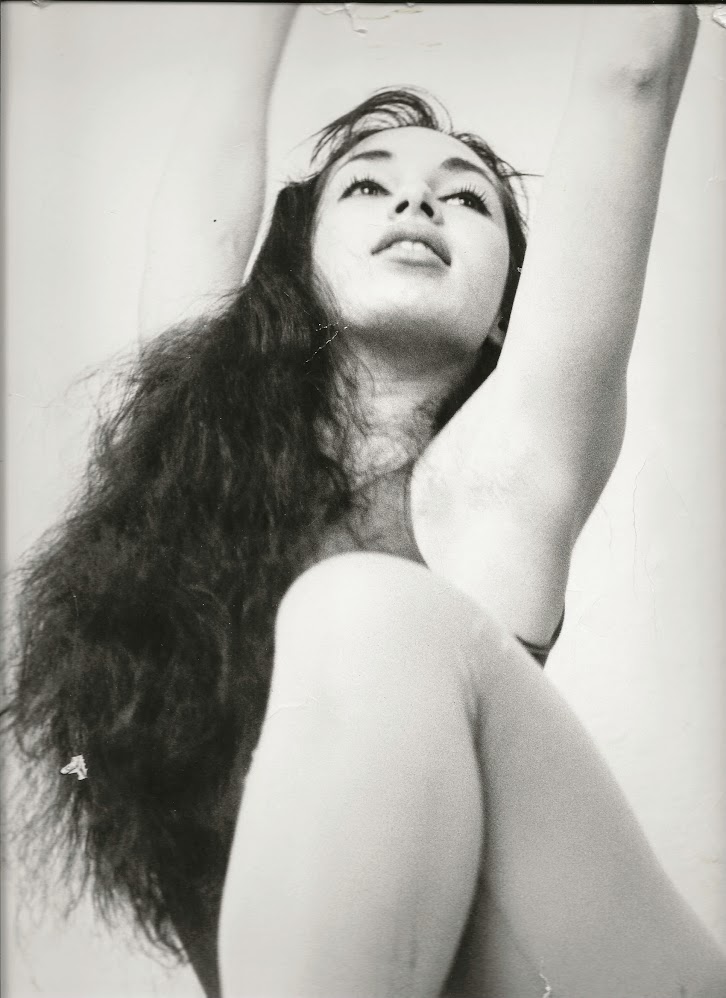 Harriet Ross is shown in a black and white photo. Her knee is in the foreground, and the phogo shows the rest of her torso and her head with her long dark dark pulled over the front of her body. Her arms are outstretched above her head, visible to the elbows, and her face is slightly upraised