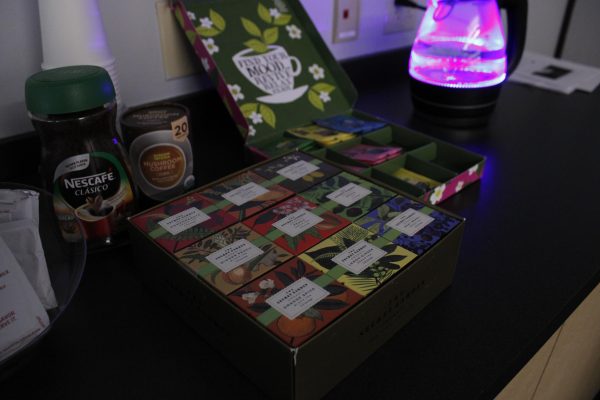A box of tea sits on a black counter next to coffee and a pink kettle.