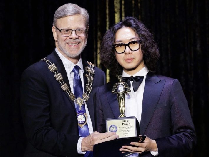 an older man presents a younger man with an award titled "First Place Close-Up Contest"
