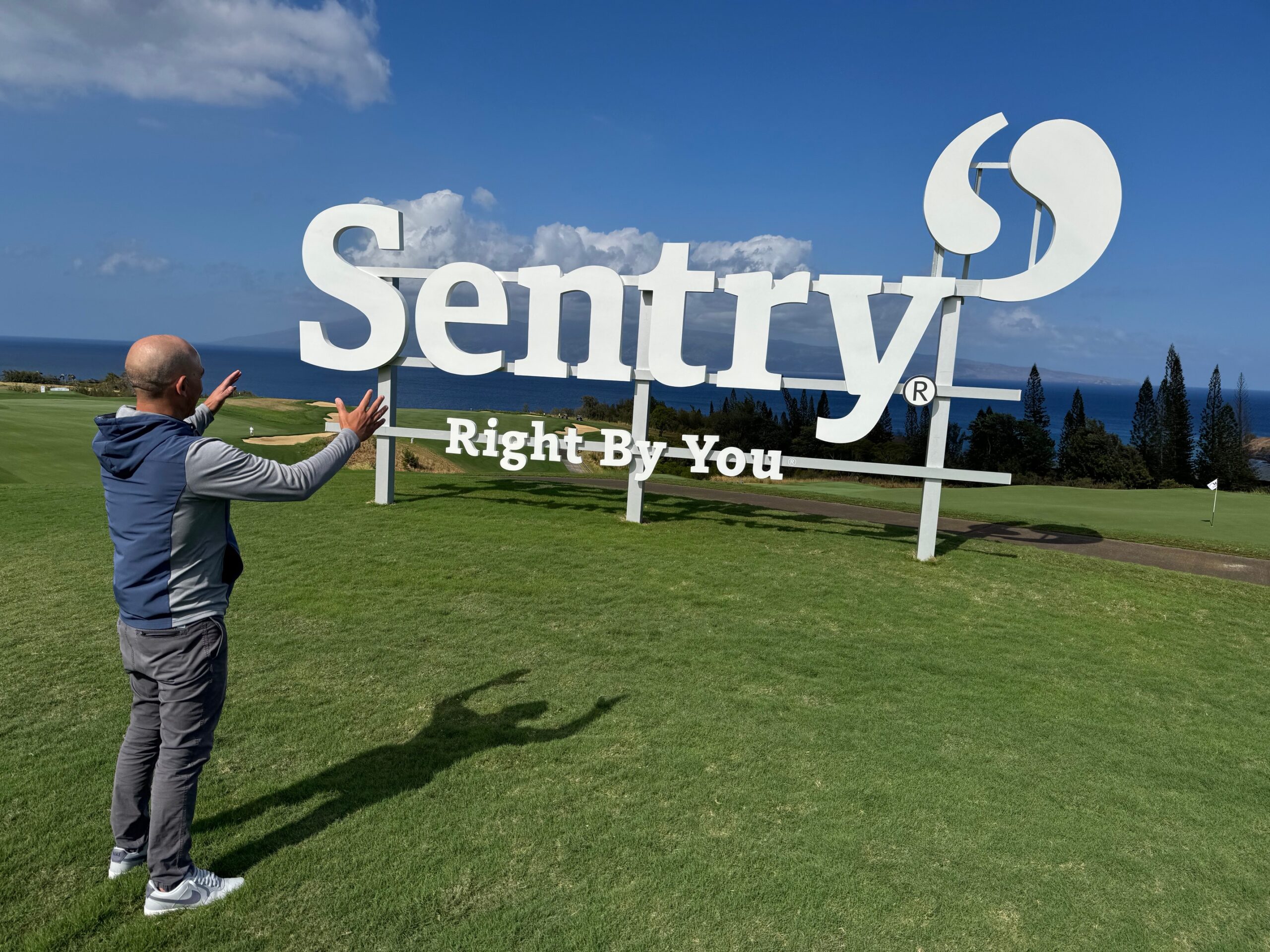 Max Novena, executive director of The Sentry golf tournament, shows off a sign nicknamed "the floating Sentry sign" near the 11th green at the Kapalua Plantation Course on Thursday. HJI / ROB COLLIAS photo