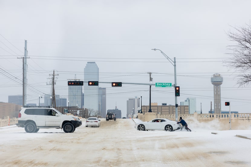 People push a car out from a slushy stretch of road nearing downtown Jan. 26, 2026 in Dallas.