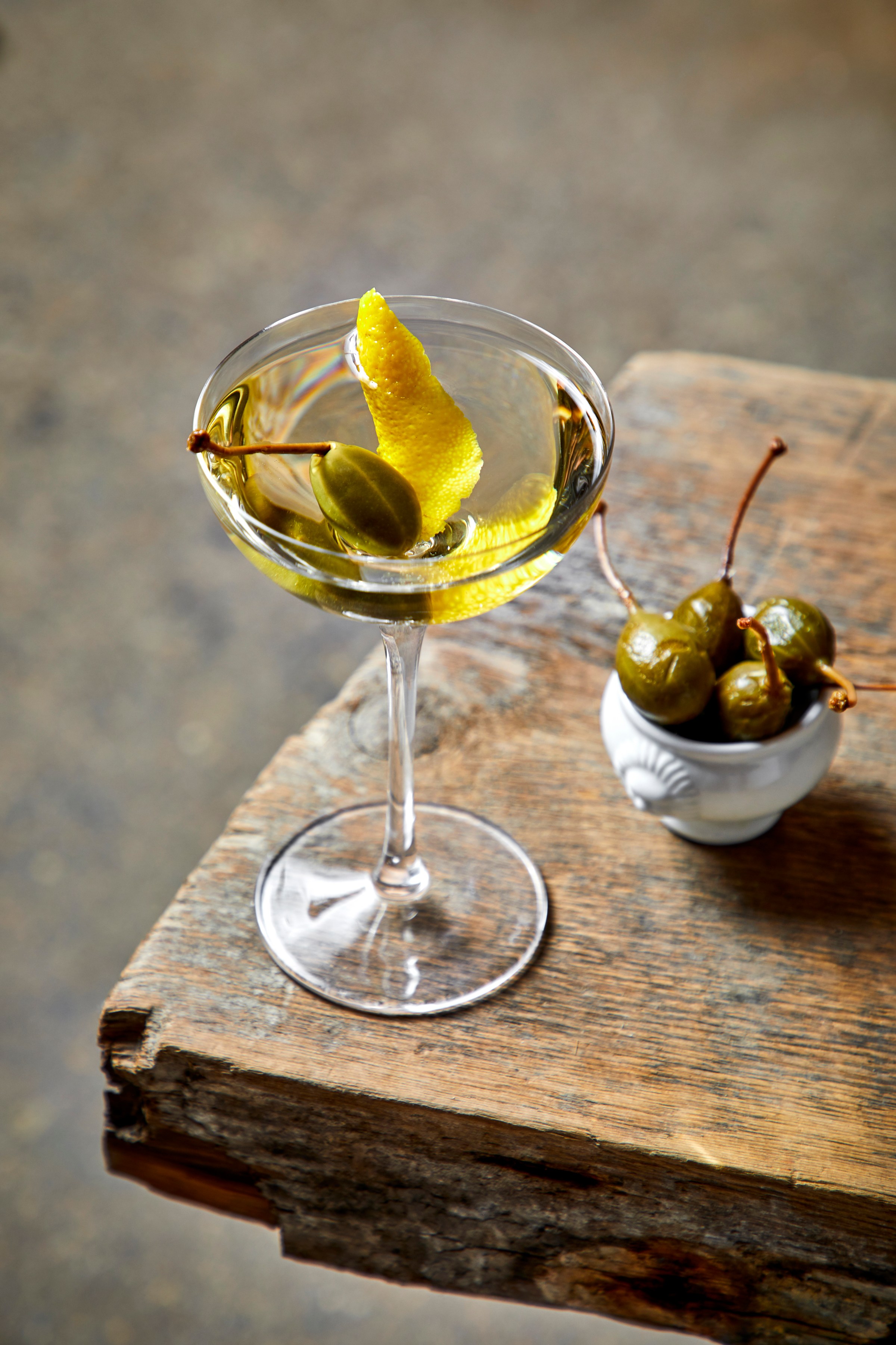 A martini with lemon rind and caper berry garnish.