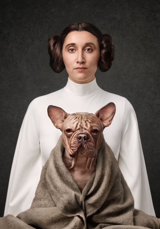 A woman in a white outfit with Princess Leia-style hair poses against a dark background, holding a French bulldog wrapped in a brown towel in her lap.