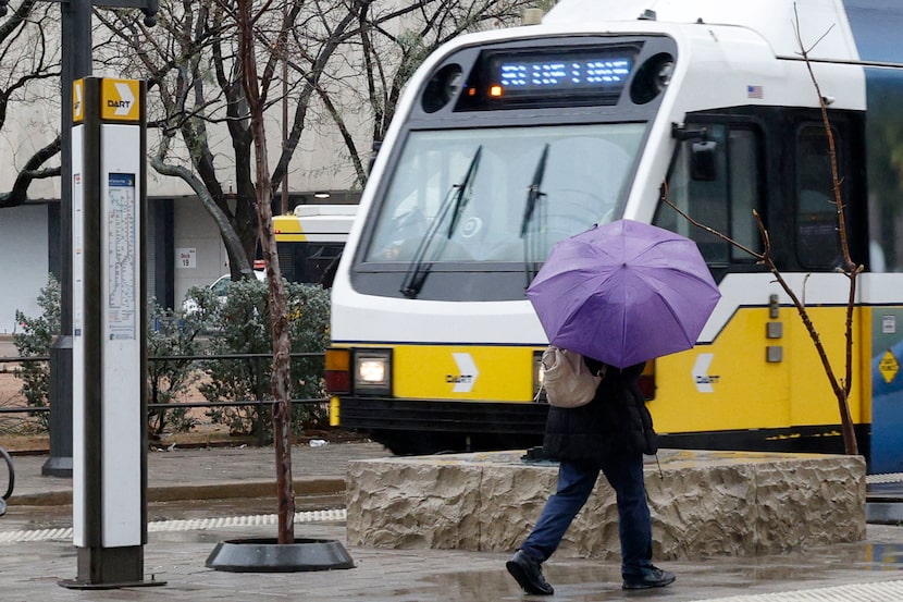 A pedestrian walks by a DART train in the rain, Friday, Jan. 23, 2026, in Dallas.