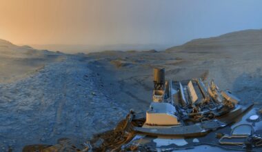 Mars rover sits on rocky terrain under a gradient sky, from orange on the left to blue on the right, with Martian hills and a dusty landscape stretching into the distance.