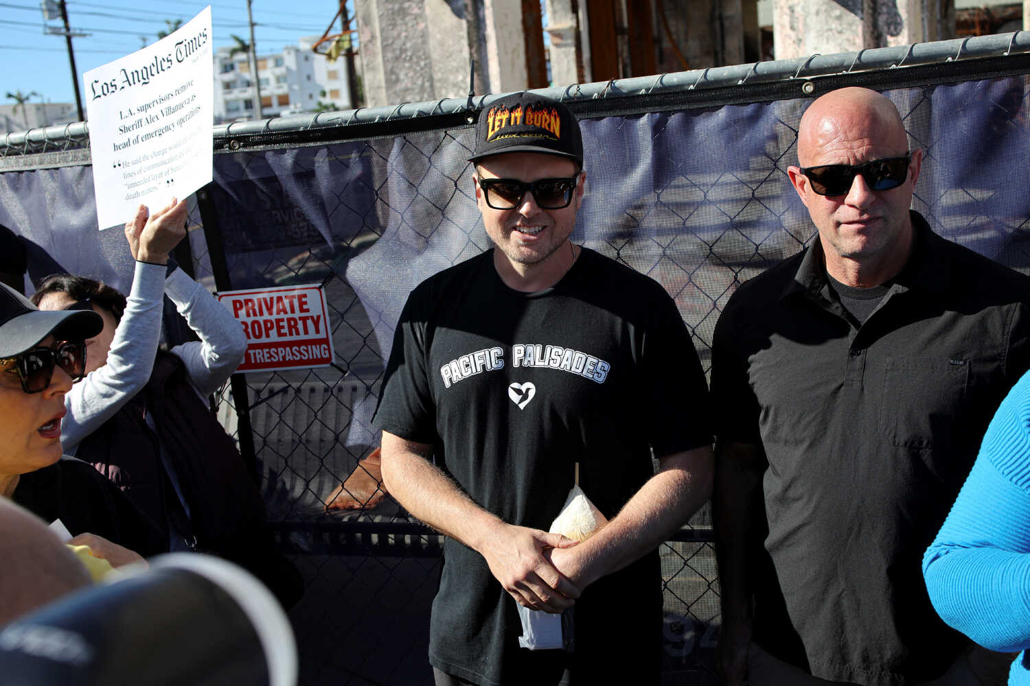 Spencer Pratt, dressed in a Pacific Palisades T-shirt, stands in front of a fence addressing a small crowd.
