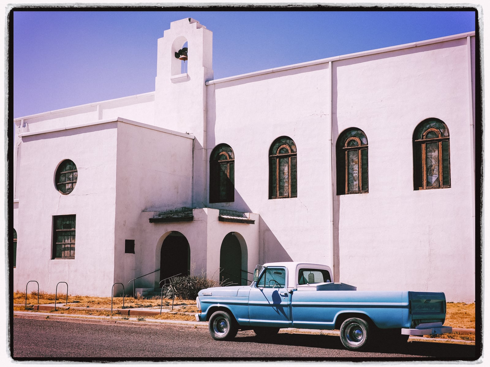 A blue truck parked in front of a white building.