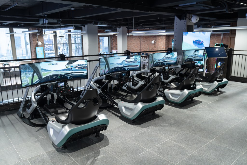 A row of sit-down race car driving simulators with wide screens.