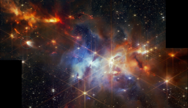 A young star-forming region is filled with wispy orange, red, and blue layers of gas and dust. At center-left, a larger star is circled. It has prominent diffraction spikes and an arc of white at right.