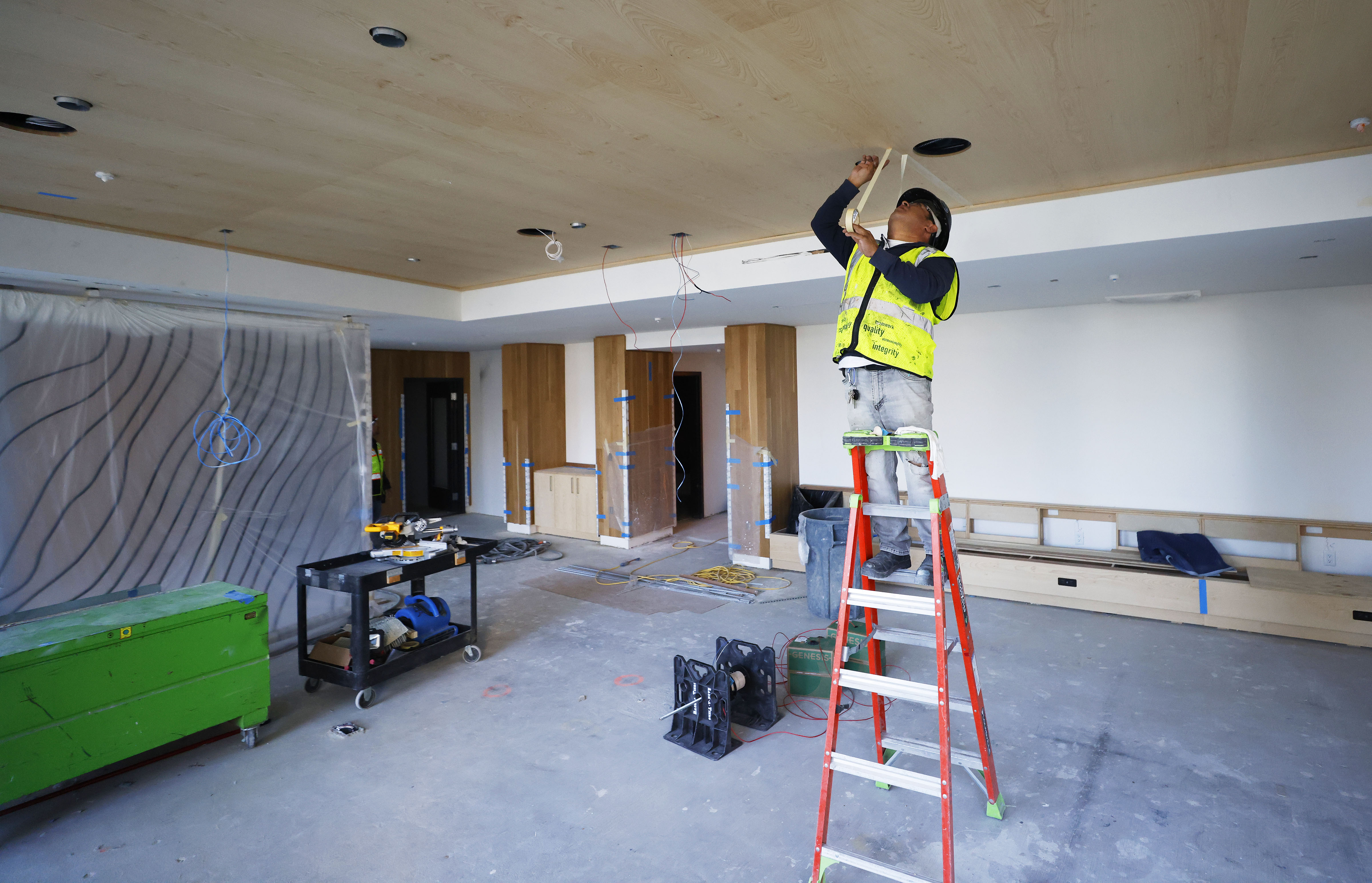 A worker installs a light fixture in a common area...