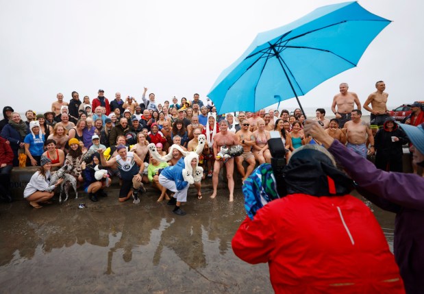 Members of the La Jolla Cove Swim Club take a photo before participating in the New Year's Day Polar Bear Plunge on a windy and rainy day at La Jolla Shores beach on Jan. 1, 2026, in San Diego. (K.C. Alfred / The San Diego Union-Tribune)