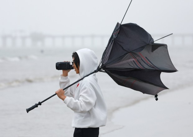 Lavy Pham, 16, takes photos in the rain of family participating in the New Year's Day Polar Bear Plunge at La Jolla Shores beach on Jan. 1, 2026 in San Diego. (K.C. Alfred / The San Diego Union-Tribune)