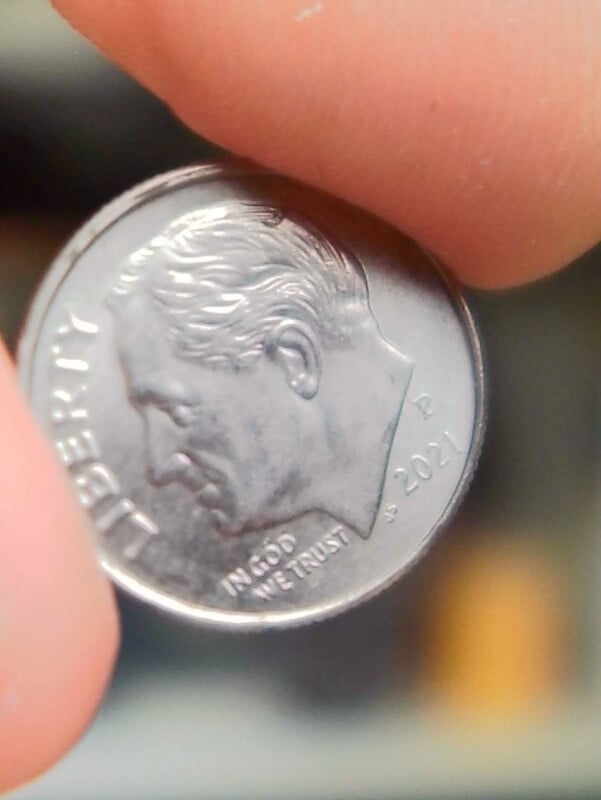 A close-up of a person holding a 2021 US dime between their fingers, showing the profile of Franklin D. Roosevelt and the word "LIBERTY" on the coin.