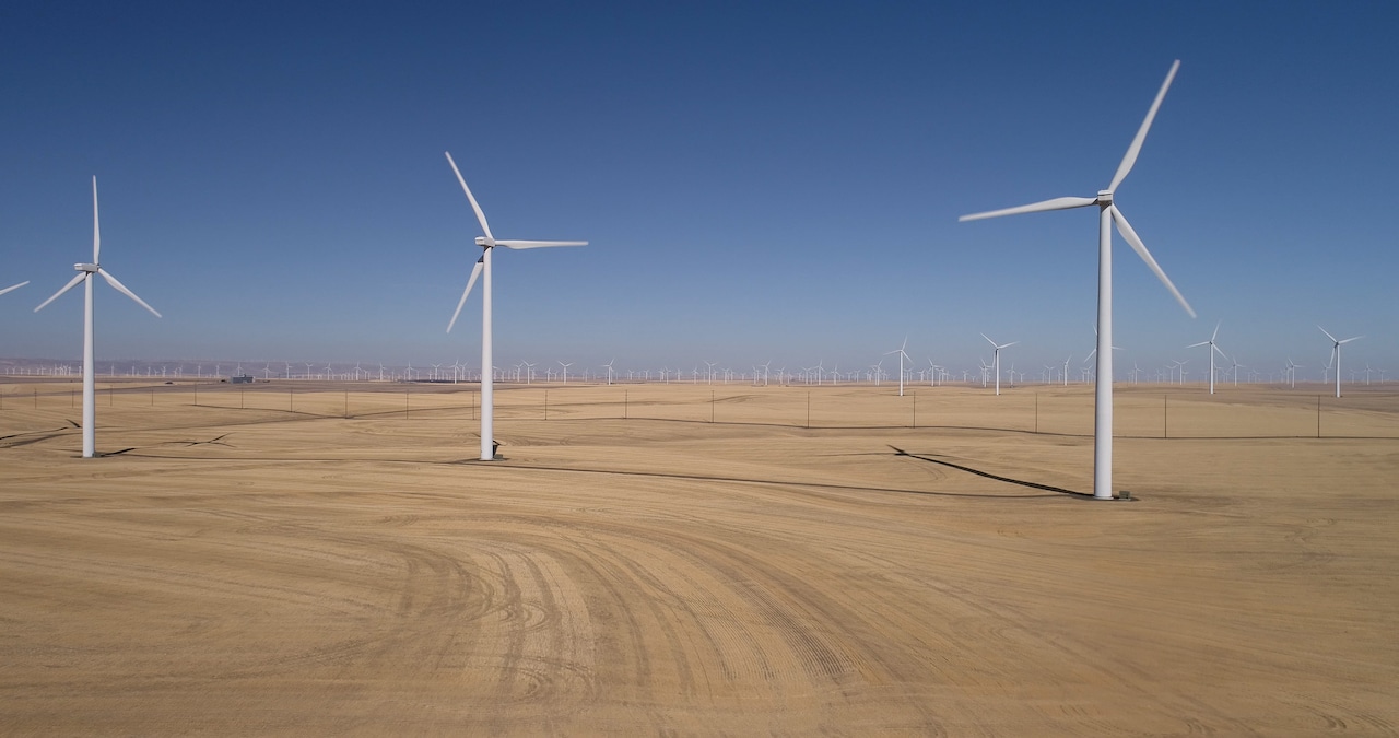 Three wind turbines, with more visible in the distance in the background, against a blue sky.