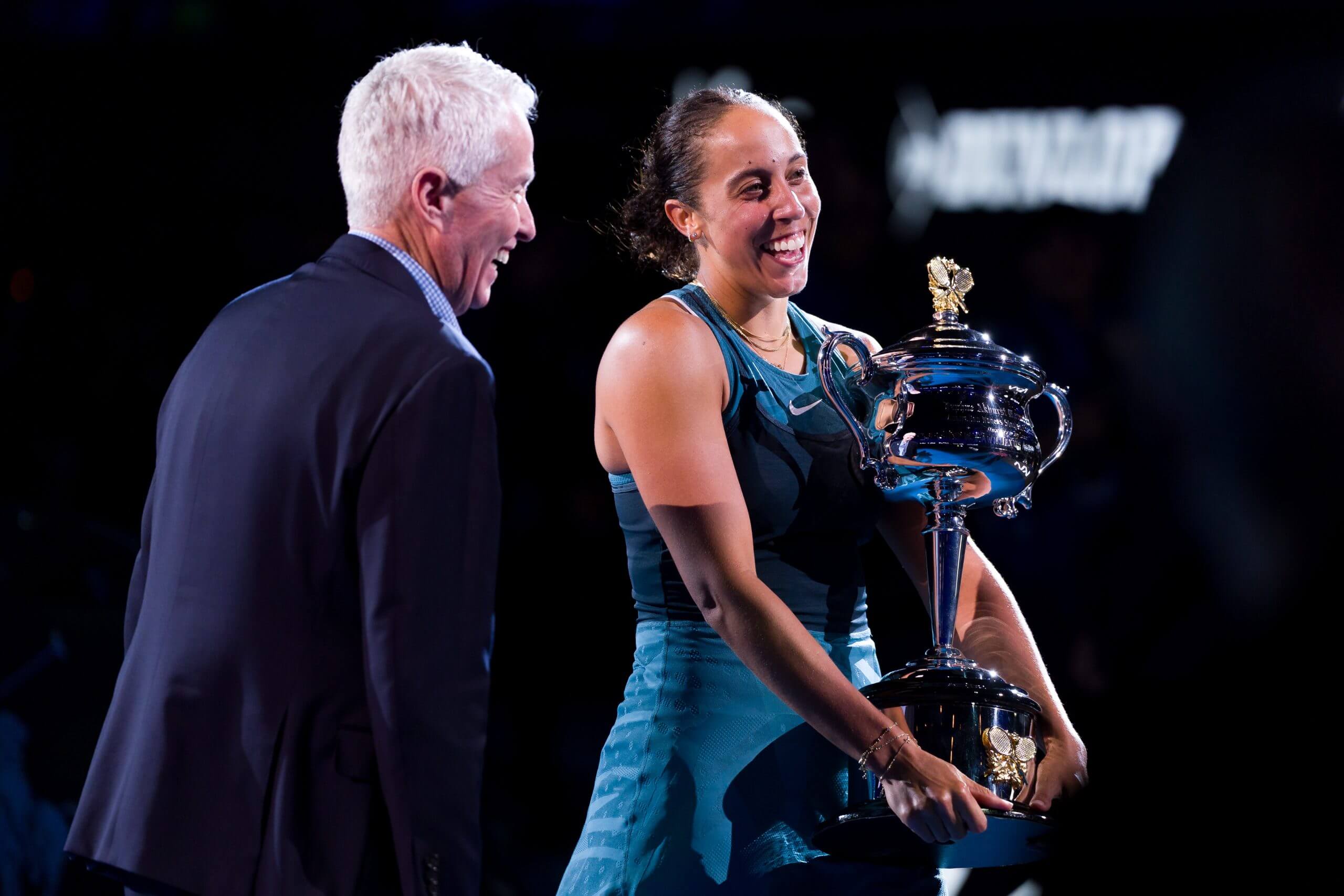 Craig Tiley, wearing a suit, smiles as he stands to the left of Madison Keys, who holds the Australian Open women's singles trophy and wears a tennis dress.