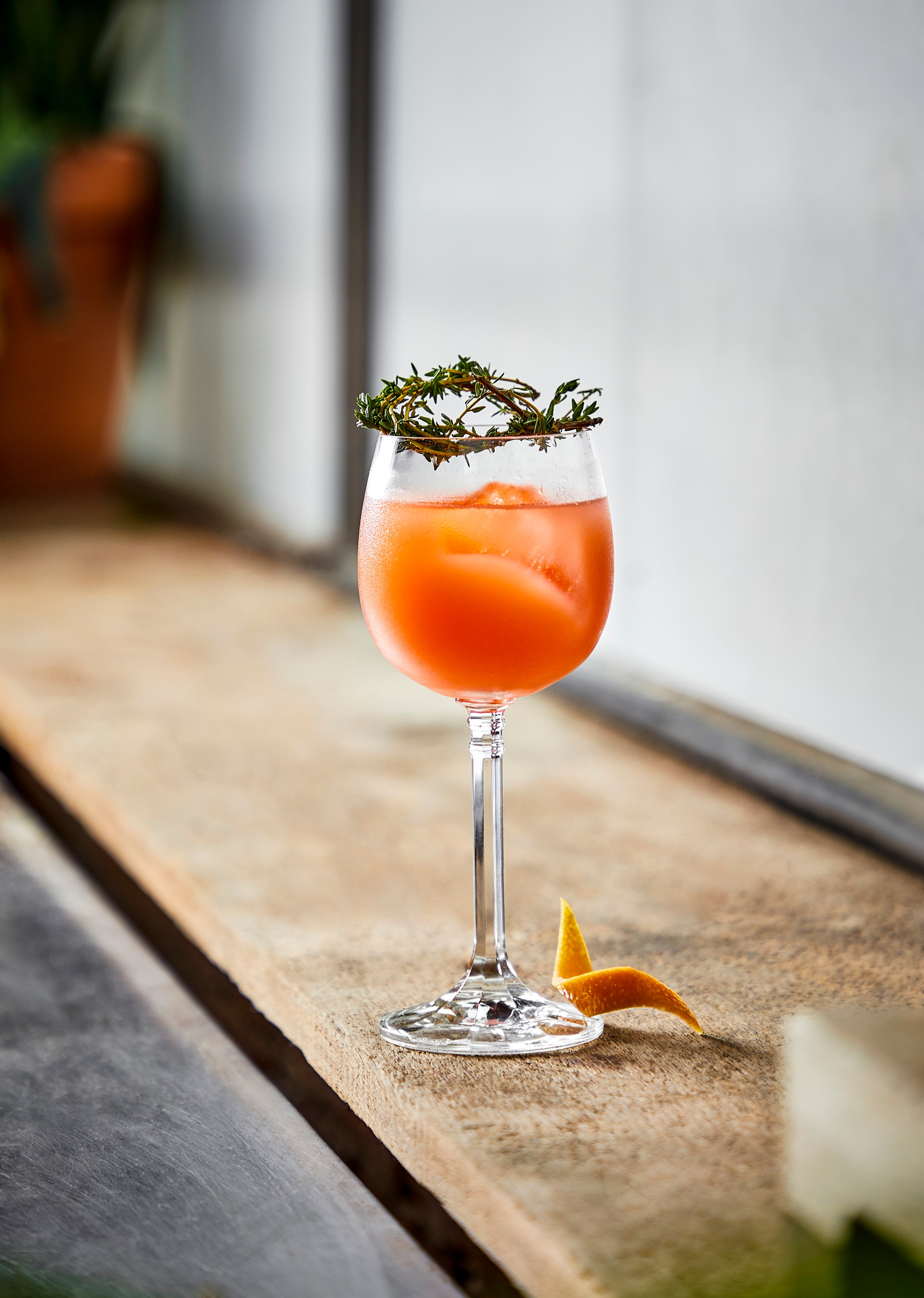 A cocktail in a wine glass with a crown of thyme sprigs.