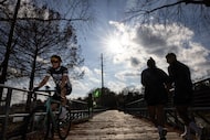 Cyclists and pedestrians wearing shorts cross a bridge at White Rock Lake on a warm Tuesday...