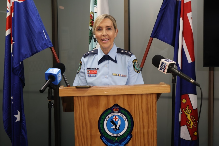 Police officer in front of microphones at stand.