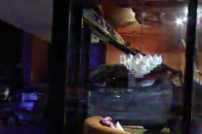 A grey four wheel drive sits among broken glass half inside a business at night.