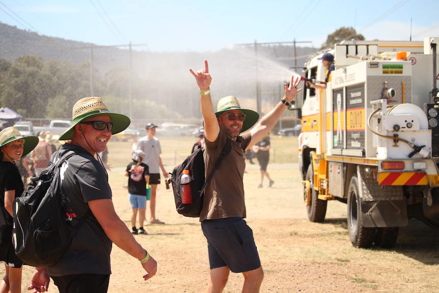 A few people wearing wide-brimmed hats laugh as a truck drives along spraying water.