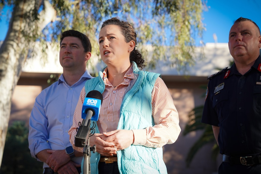 A woman talking into an ABC News microphone, with two police officers standing either side of her.