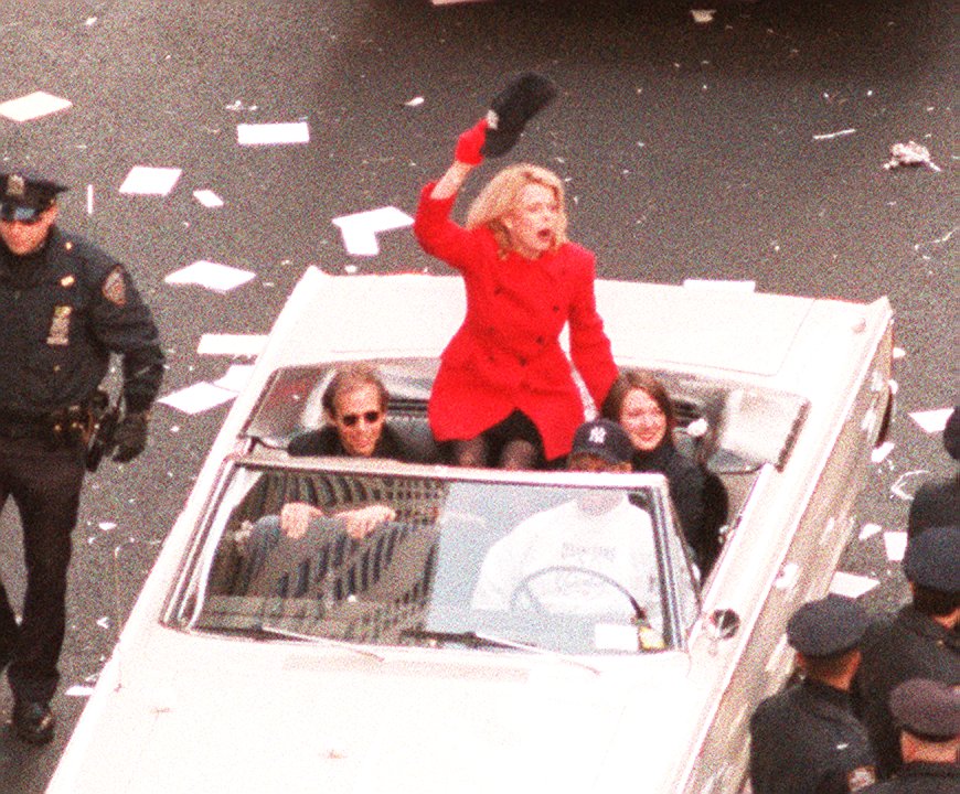 Betsy McCaughey Ross in a red coat waving from a car at the Yankees World Series Parade.