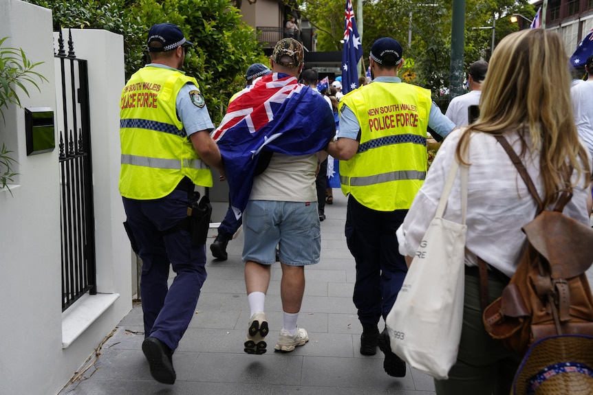 Two police officers escorting someone in an Australian flag away