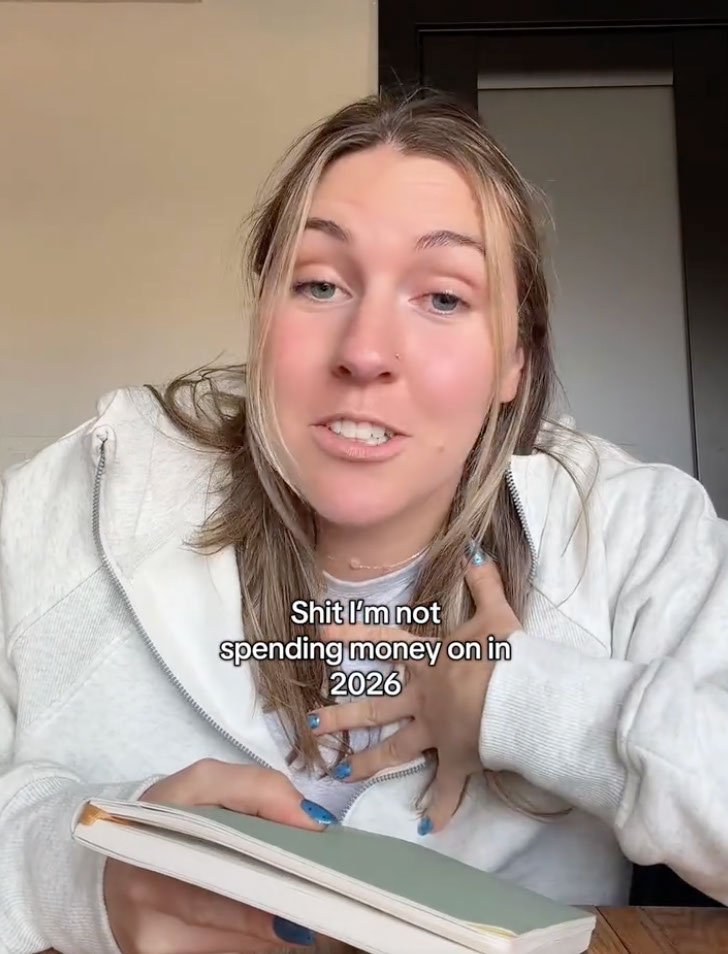A young woman holding a notebook with text overlay "Shit I'm not spending money on in 2026."