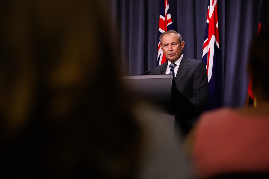 Two men in suits hold a press conference at a lecturn in a conference room