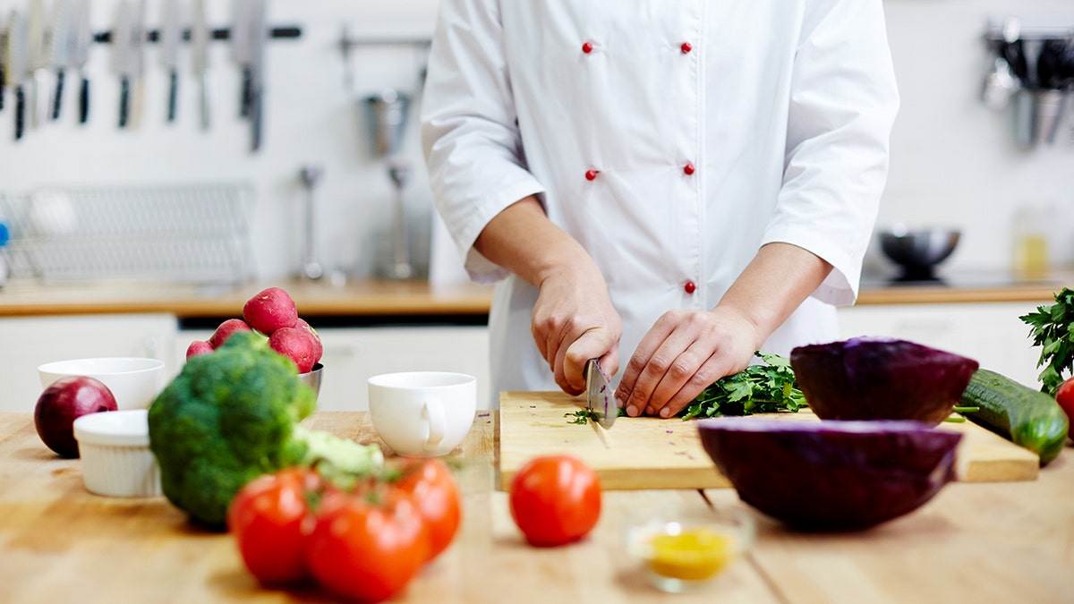A chef wearing a chef's apron chops vegetables on a cutting board in a kitchen.