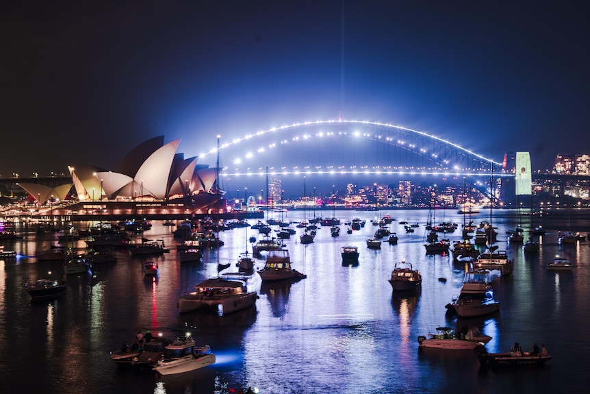 The Sydney Harbour Bridge illuminated with white lights with a menorah on the pylons with boats in the water.