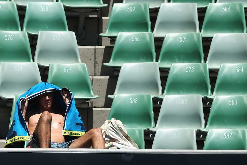 A man holds a towel up over himself while seated in the stadium at the Australian Open in 2014.