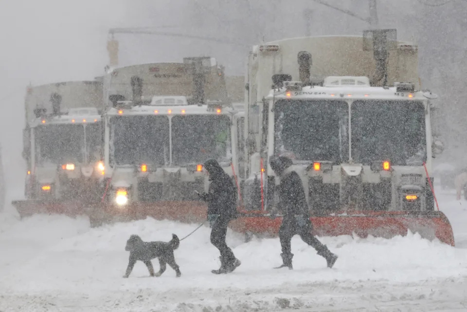 People cross a street as trucks plow snow in the Manhattan borough of New York City on January 25, 2026.