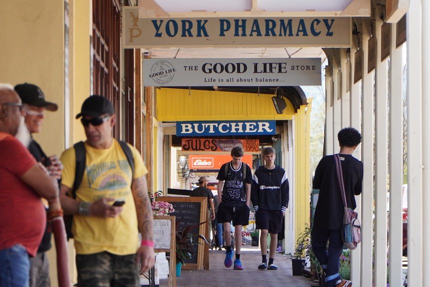 People walk down a covered pavement on a country street lined with shops.