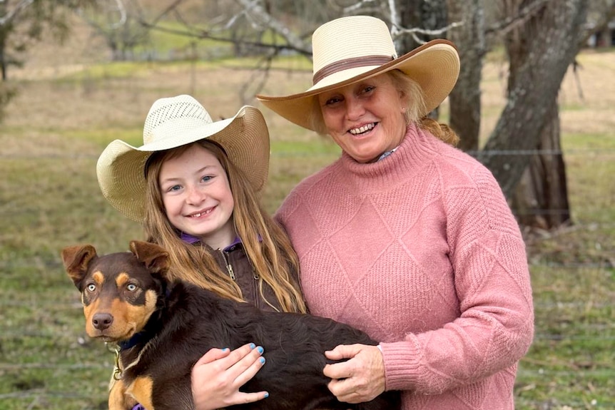 A young girl stands with a woman, holdiner her Kelpie puppy.