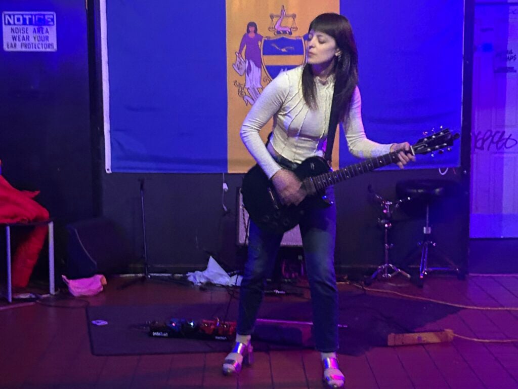 Emily Robb playing the guitar with her eyes closed during a solo performance on the floor of a bar