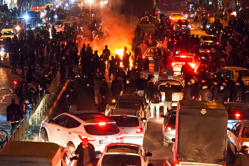 Crowds of people on a road around a fire with cars surrounding them