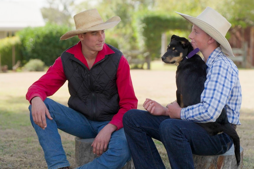 A young man sits next to a boy holding a Kelpie puppy on his lap.