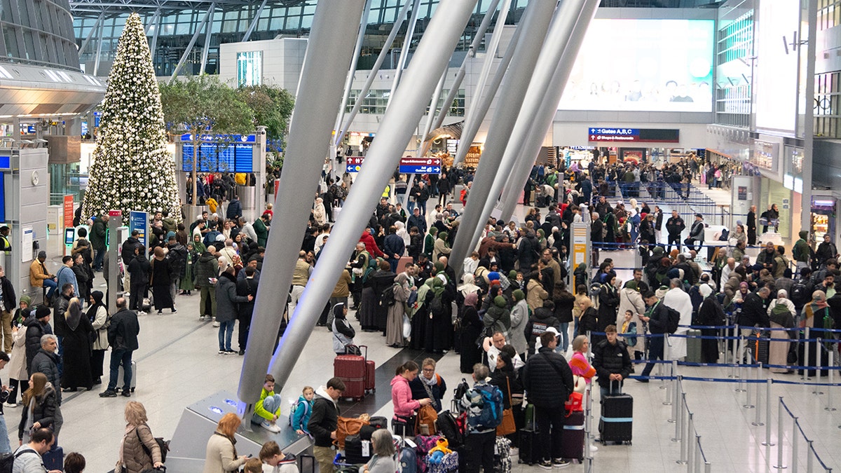Crowded airport terminal decorated with a large illuminated Christmas tree as travelers wait in long lines during the holiday season.